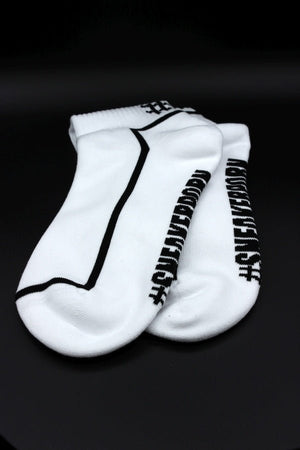 Ein Paar Sk8erboy® #SNEAKERPORN Socken schwarz, mit schwarzem Stoff und auffälligem Sk8erboy® Branding an den Seiten, auf einem schlichten schwarzen Hintergrund.